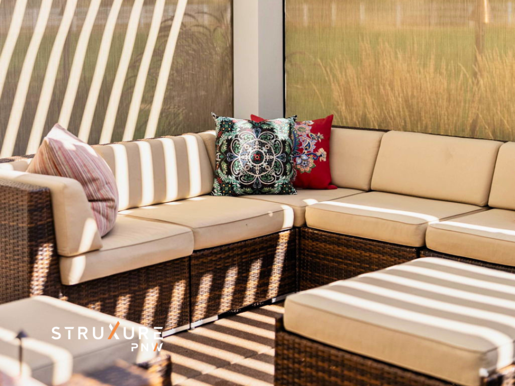 Sectional couch with dappled light streaming through an opened white aluminum StruXure louvered pergola above with tan screens lowered and visible behind the couch creating a screened in porch feel