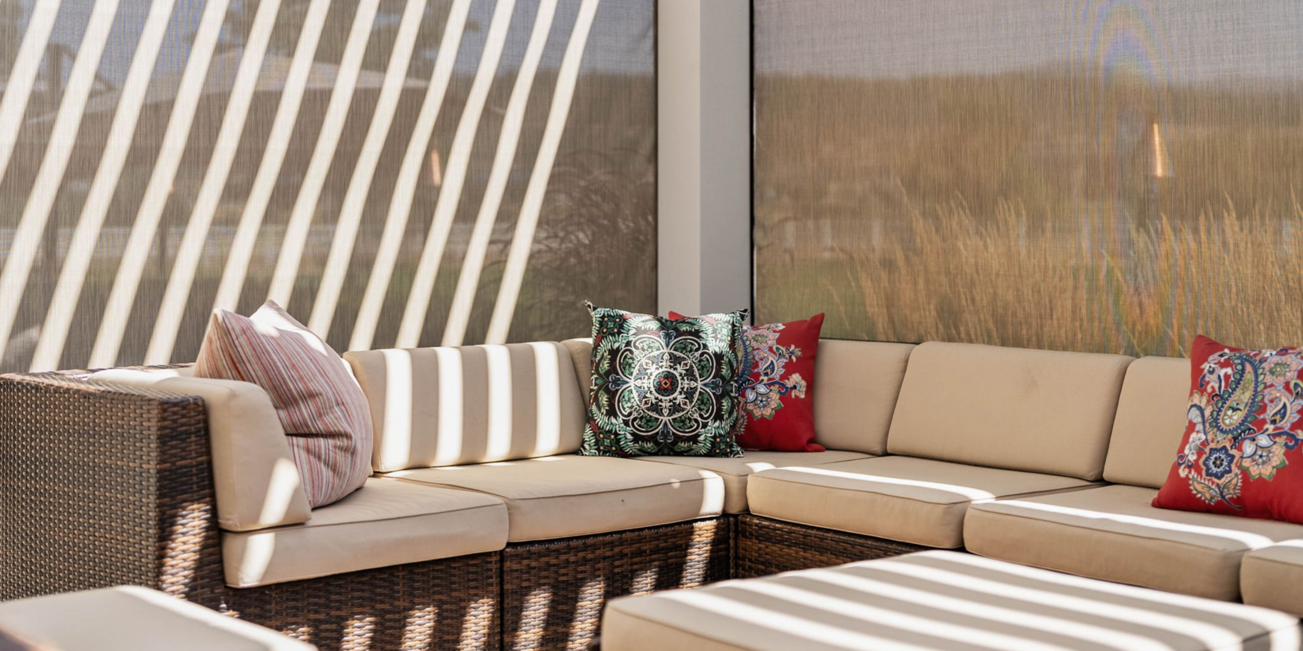 Sectional couch with dappled light streaming through an opened white aluminum StruXure louvered pergola above with tan screens lowered and visible behind the couch creating a screened in porch feel